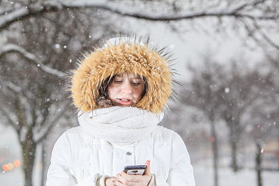 漂亮的少女在下雪的时候用智能手机发短信