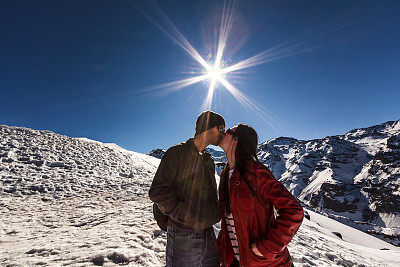 一对情侣在明亮的太阳下亲吻雪山