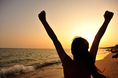 欢呼的女人在海边向夕阳张开双臂
