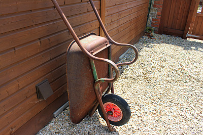 旧生锈的金属手推车靠在木制的花园棚子上，形象