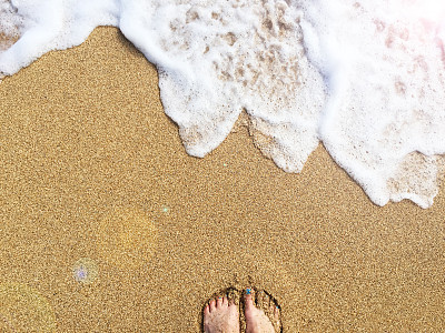 在夏威夷考艾岛的金色沙滩上，女性的脚在沙子里