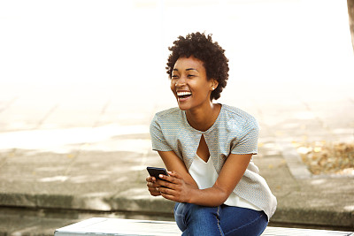 美丽年轻的非洲女人在外面微笑着拿着手机