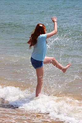 一个女孩在海滩上玩耍,溅起水花,在大海里嬉戏 一个女孩在海滩上玩耍,溅起水花,在大海里嬉戏