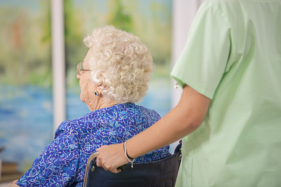 护理护士帮助坐轮椅的老人。后面的观点。