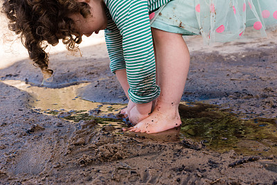 光着脚蹒跚学步的孩子在沙子和水里玩耍