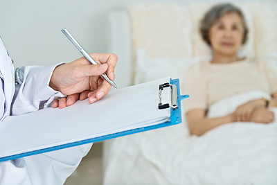 医生在写字板上写字，年长的女病人在床上