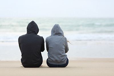 两个悲伤的青少年坐在海滩上