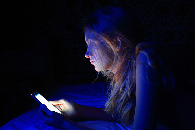 年轻女子睡前在床上玩智能手机