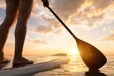 在平静的海面上站立划桨，双腿特写，日落