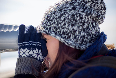 一名年轻的女游客在冬天用望远镜看雪天