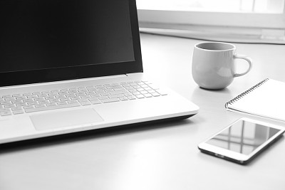 商务笔记本电脑与智能手机，笔记本纸笔记信息和一杯咖啡在木书桌背景(软焦点黑白照片)