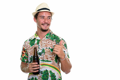 体贴的年轻快乐的游客男子微笑和给予拇指，同时拿着一瓶啤酒孤立的白色背景