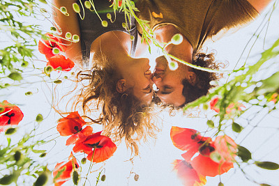 春天里，一对年轻幸福的夫妇卷着头发，欣赏着盛开的红黄相间的罂粟花