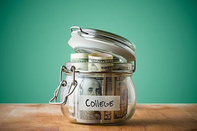 在绿色背景上孤立的玻璃罐中的美元。为上大学省钱的概念。