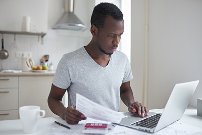 专注的年轻非洲裔美国学生使用网上银行应用，手放在触控板上，看着他的笔记本电脑屏幕，试图支付大学教育。财务问题