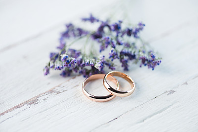 金色的结婚戒指和美丽的小蓝花在木制桌面的特写