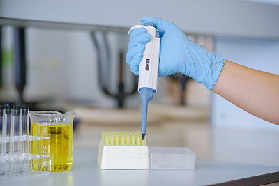 在化学实验室使用自动吸管工作的科学家。穿蓝色的手套。