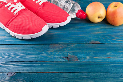 健康的生活方式的背景。木制背景上的运动鞋、一瓶水和苹果。健康与运动生活的概念。俯视图