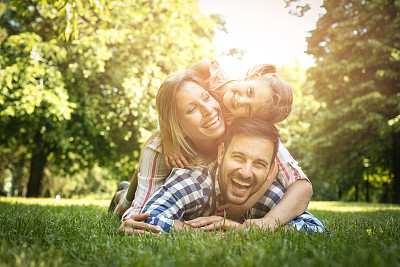 快乐的家庭一起享受在夏天的日子。一家人躺在草地上。母亲和女儿躺在父亲的背上。