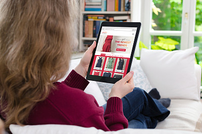 金发女人坐在家里的沙发上，正在看一个数字网站上的网上购物