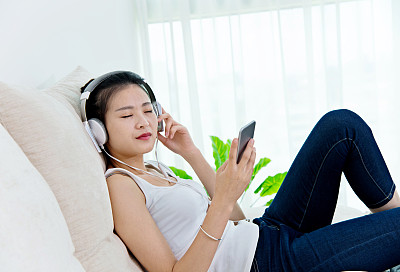年轻女子在沙发上听着手机里的音乐