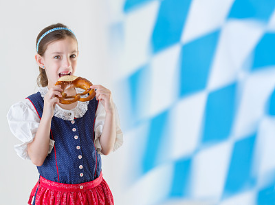 巴伐利亚小女孩穿着传统连衣裙吃椒盐卷饼