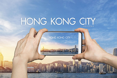 日出时分，一名女孩在香港维多利亚港用手机拍照