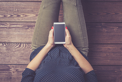 一名年轻女子坐在地板上使用智能手机的照片