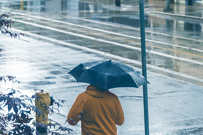 一个男人的后视图行走在雨中,拿着和伞