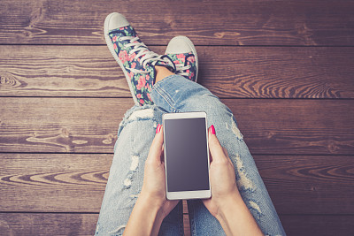 女人拿着现代白色智能手机黑色空屏幕在木地板上