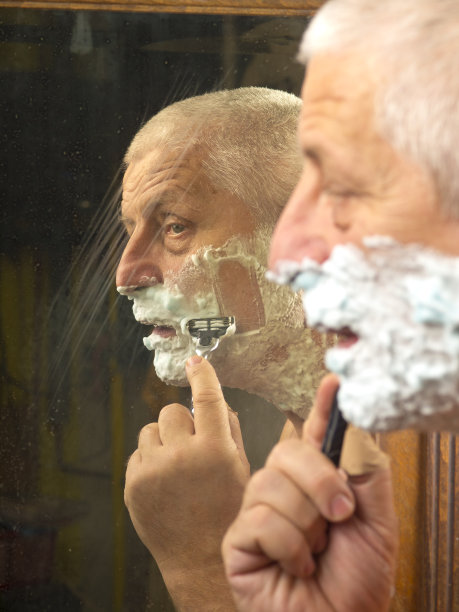 在浴室镜子前刮胡子的男性