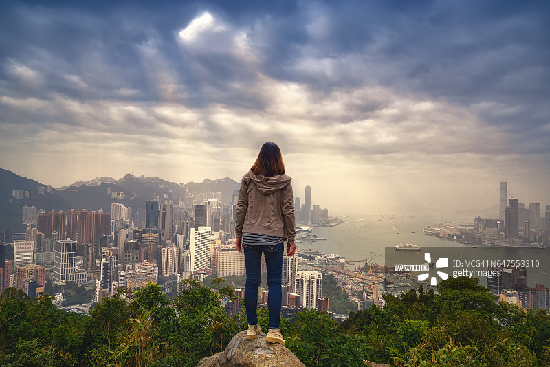 女孩与背包客享受阳光在山顶雾蒙蒙的城市.