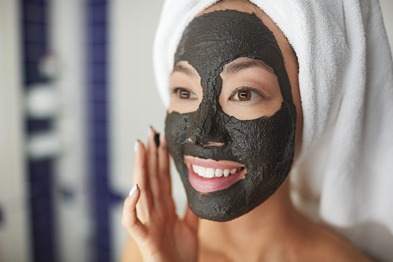 Closeup,portrait,of,beautiful,Asian,woman,applying,face,mask,during,beauty,treatment,routine??,in,bathroom,??,looking,in,mirror,and,smiling