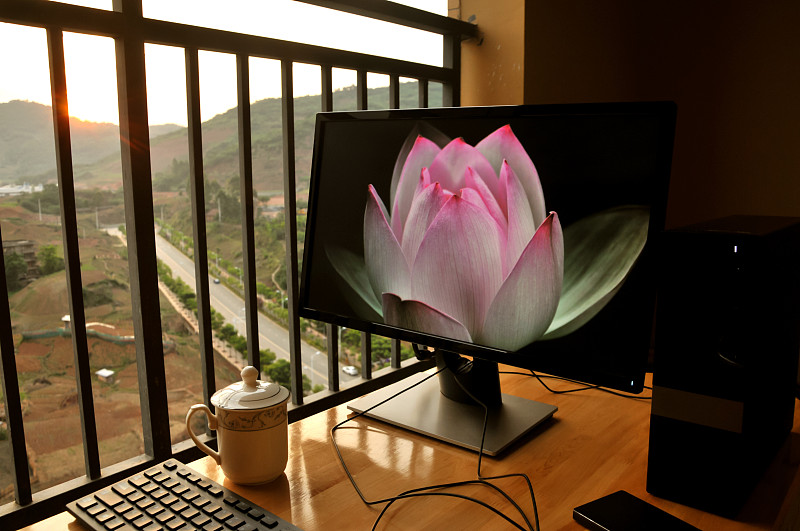 Computer,with,my,lotus,flower,image、Tea,cup,and,telephone,on,black,wood,table,sun,rising.